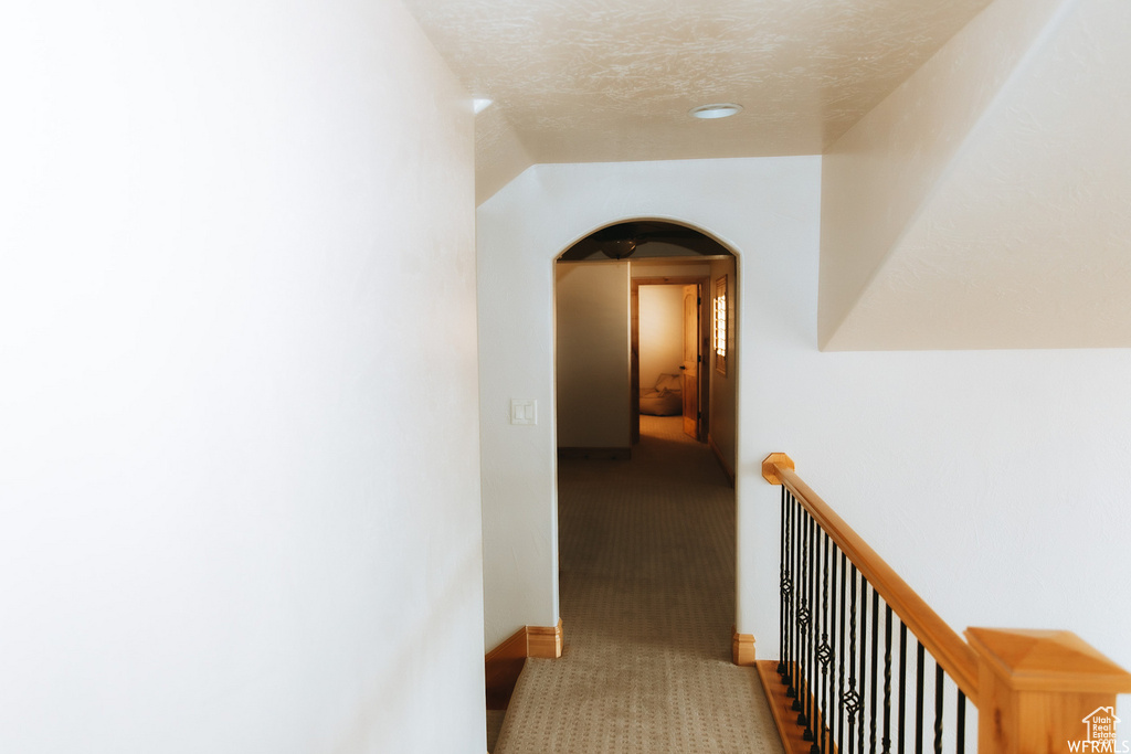 Corridor featuring a textured ceiling and dark carpet