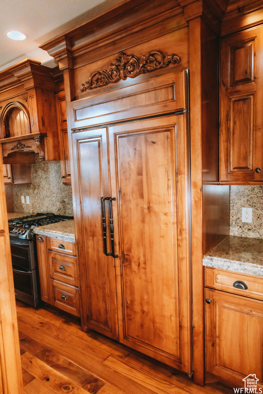 Kitchen with range with two ovens, backsplash, hardwood / wood-style floors, and light stone counters