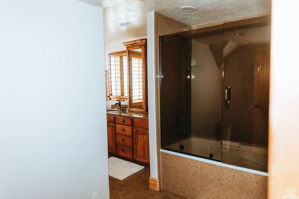 Bathroom featuring enclosed tub / shower combo, vanity, tile floors, and a textured ceiling