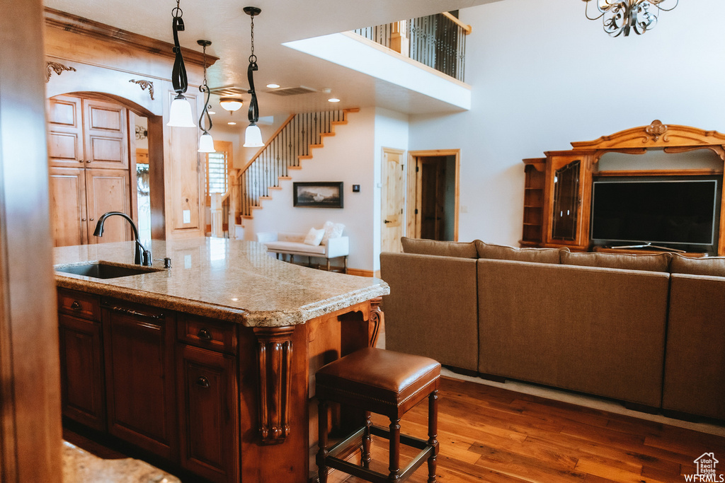 Kitchen featuring sink, dark hardwood / wood-style floors, a center island with sink, pendant lighting, and light stone countertops