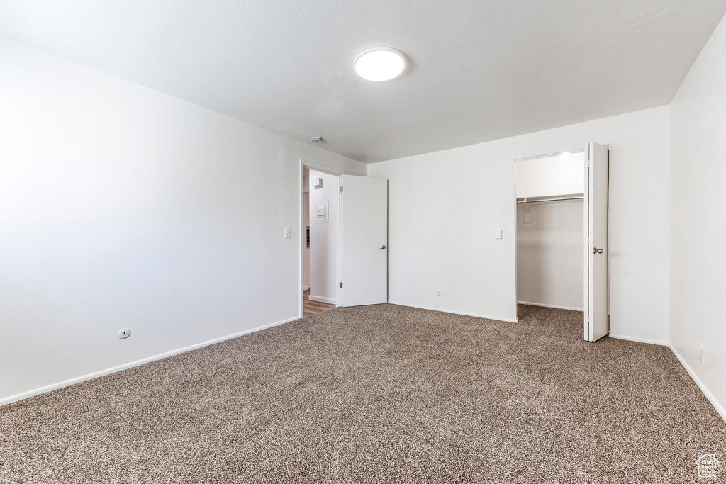 Unfurnished bedroom with a closet, dark carpet, and a walk in closet
