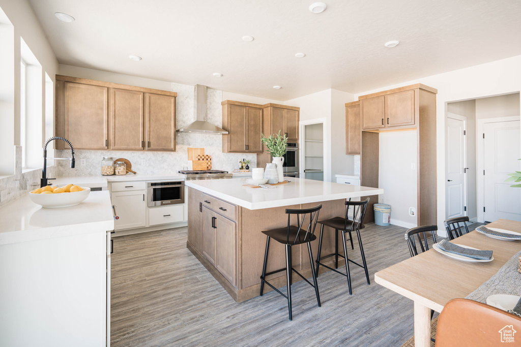 Kitchen with a center island, tasteful backsplash, light hardwood / wood-style flooring, and wall chimney range hood