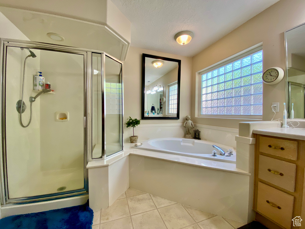 Bathroom with vanity with extensive cabinet space, tile floors, independent shower and bath, and a textured ceiling