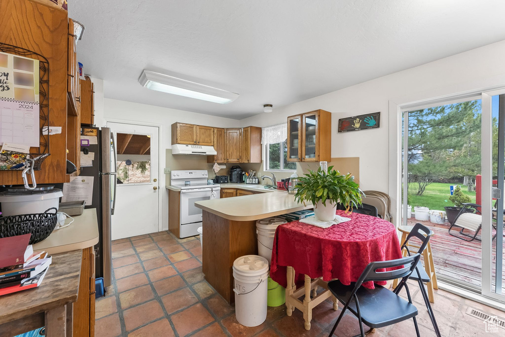 Kitchen featuring kitchen peninsula, electric range, dark tile flooring, stainless steel fridge, and sink