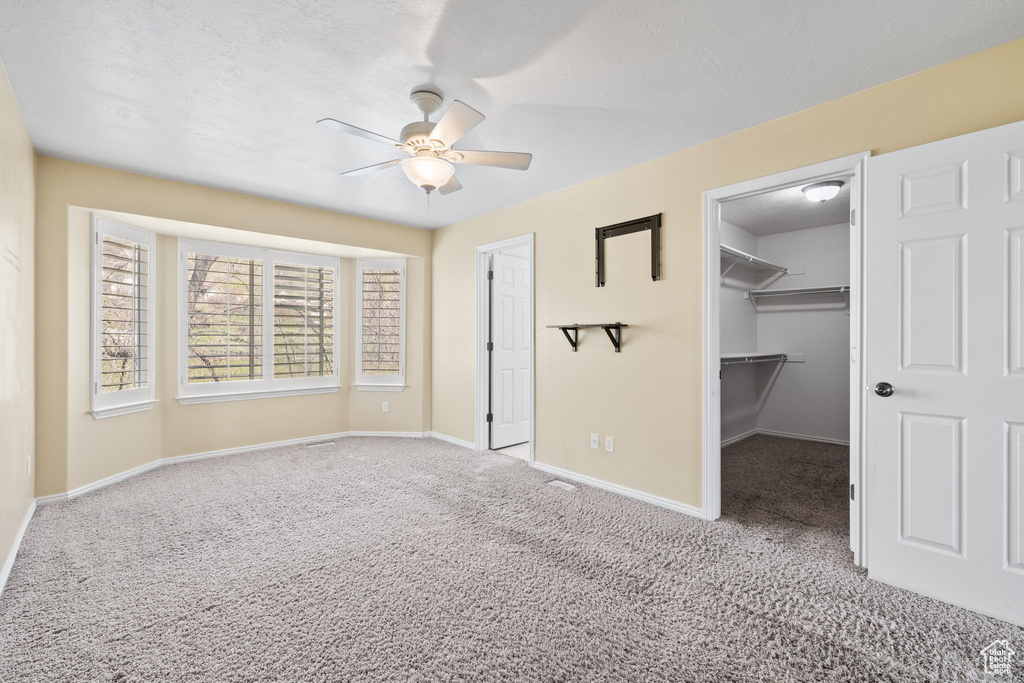 Unfurnished bedroom with ceiling fan, a spacious closet, light carpet, and a closet