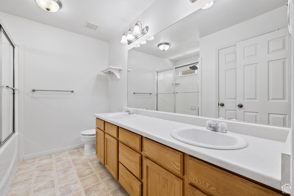 Full bathroom featuring tile flooring, double sink vanity, toilet, and bath / shower combo with glass door