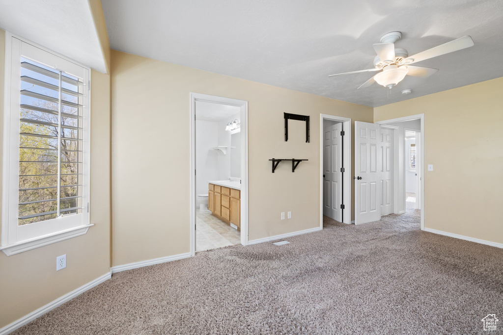 Unfurnished bedroom with ceiling fan, a walk in closet, light colored carpet, and ensuite bath