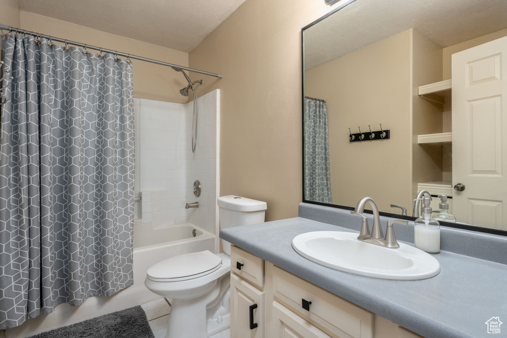Full bathroom with tile flooring, a textured ceiling, oversized vanity, shower / bath combination with curtain, and toilet