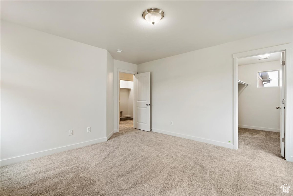 Unfurnished bedroom with light carpet, a closet, and a walk in closet