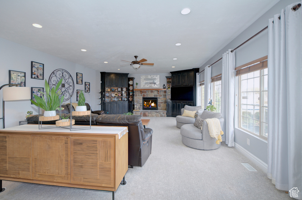Carpeted living room featuring ceiling fan and a stone fireplace