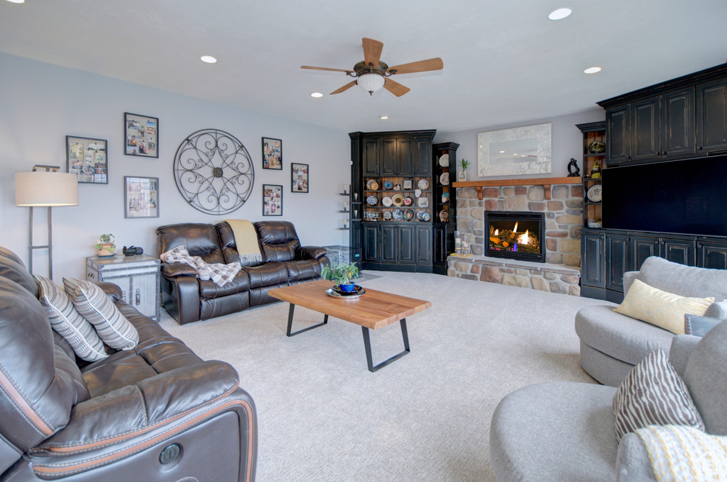 Living room with a stone fireplace, light colored carpet, and ceiling fan