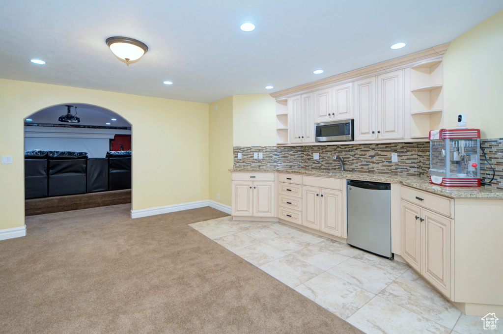 Kitchen with backsplash, stainless steel appliances, light tile flooring, light stone counters, and sink