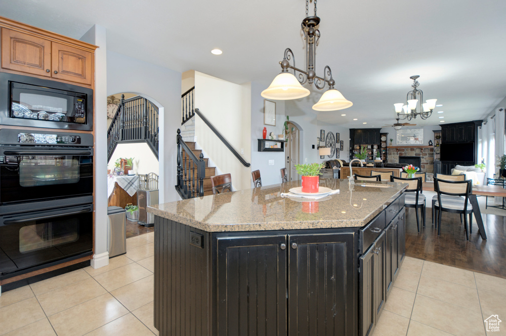 Kitchen with decorative light fixtures, black appliances, an island with sink, a fireplace, and light wood-type flooring