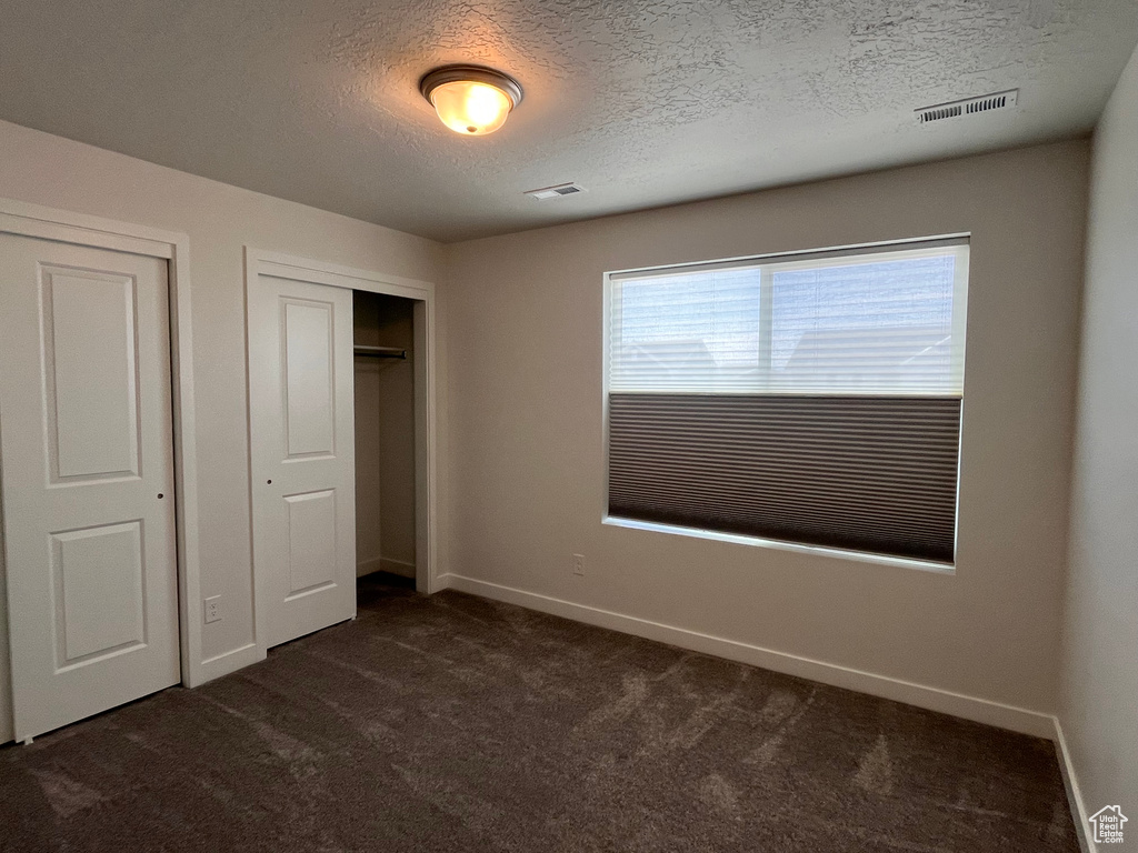 Unfurnished bedroom with dark colored carpet, a closet, and a textured ceiling