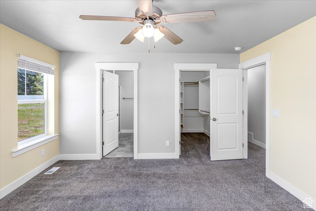Unfurnished bedroom featuring a walk in closet, ceiling fan, and dark carpet