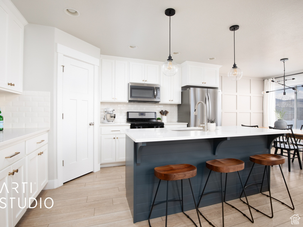 Kitchen featuring appliances with stainless steel finishes, tasteful backsplash, a breakfast bar, and decorative light fixtures