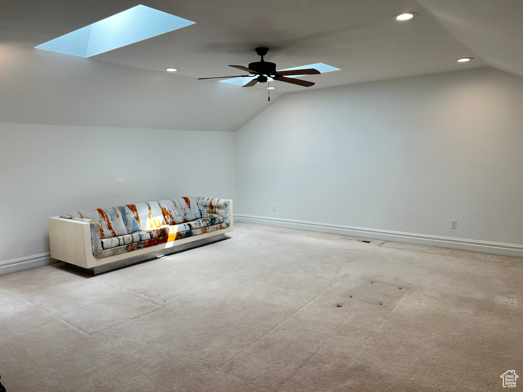 Unfurnished living room featuring light colored carpet, lofted ceiling with skylight, and ceiling fan