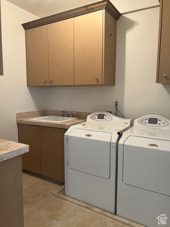 Laundry area with dark tile floors, washing machine and clothes dryer, cabinets, and sink