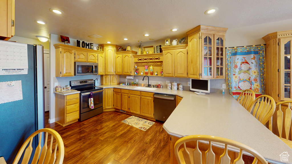 Kitchen with dark wood-type flooring, backsplash, kitchen peninsula, stainless steel appliances, and sink