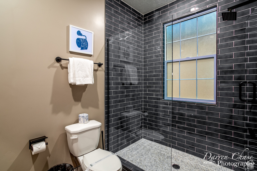 Bathroom featuring a wealth of natural light, tiled shower, and toilet