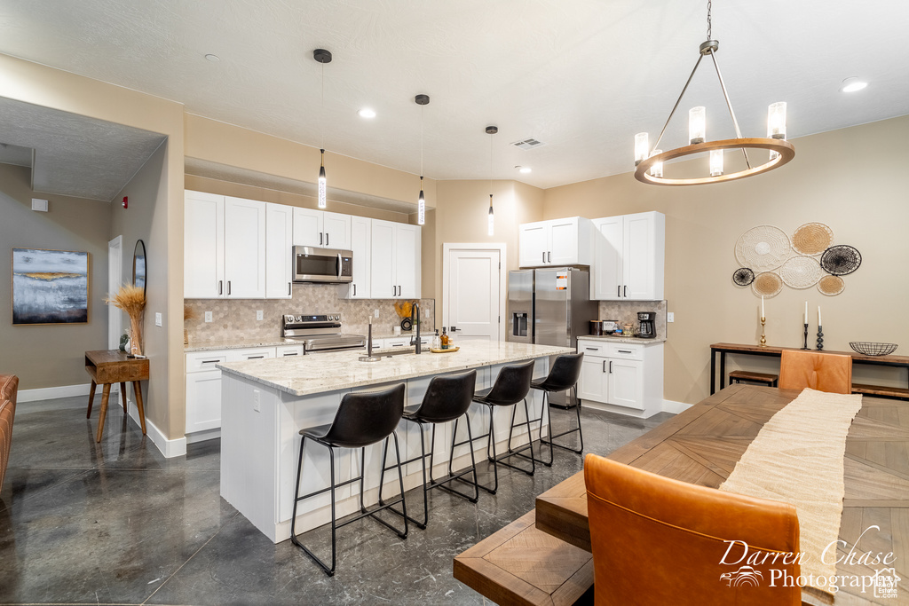 Kitchen featuring decorative light fixtures, a kitchen island with sink, backsplash, and stainless steel appliances