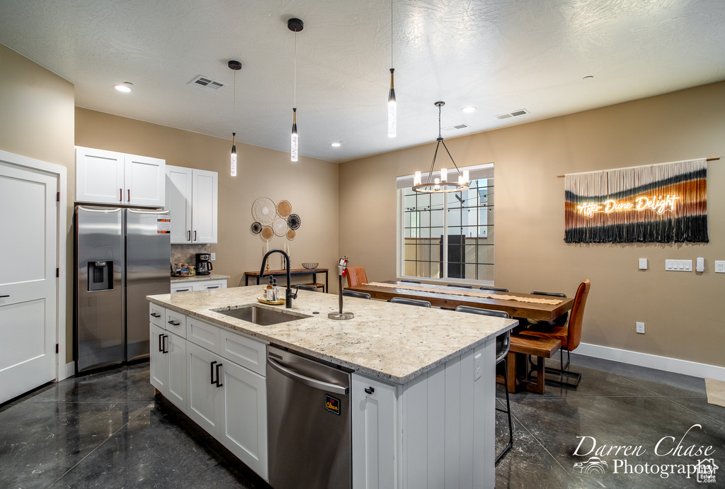 Kitchen with a center island with sink, appliances with stainless steel finishes, white cabinetry, and pendant lighting