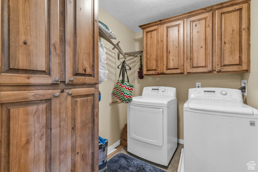 Clothes washing area with tile flooring, cabinets, a textured ceiling, and washer and clothes dryer