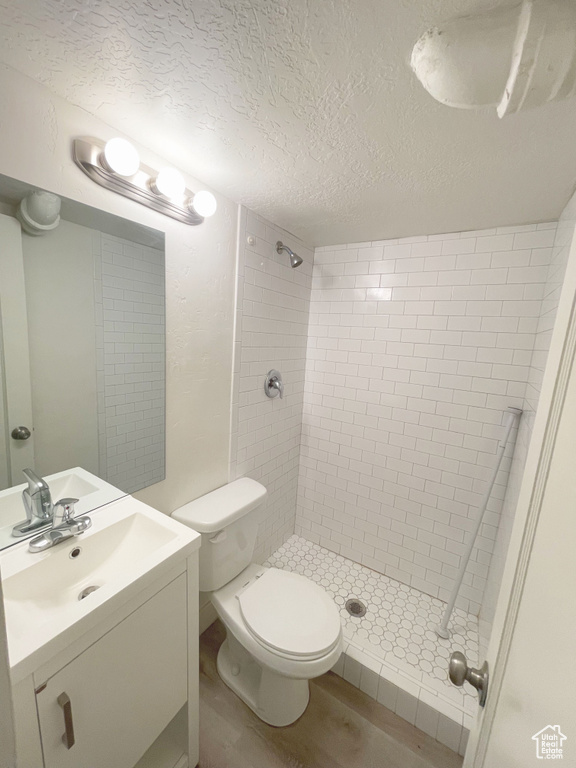 Bathroom with tiled shower, a textured ceiling, hardwood / wood-style floors, toilet, and vanity