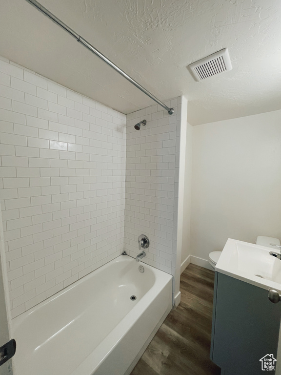 Full bathroom with tiled shower / bath, a textured ceiling, hardwood / wood-style floors, toilet, and vanity