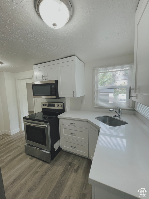 Kitchen with sink, appliances with stainless steel finishes, white cabinetry, and dark hardwood / wood-style floors