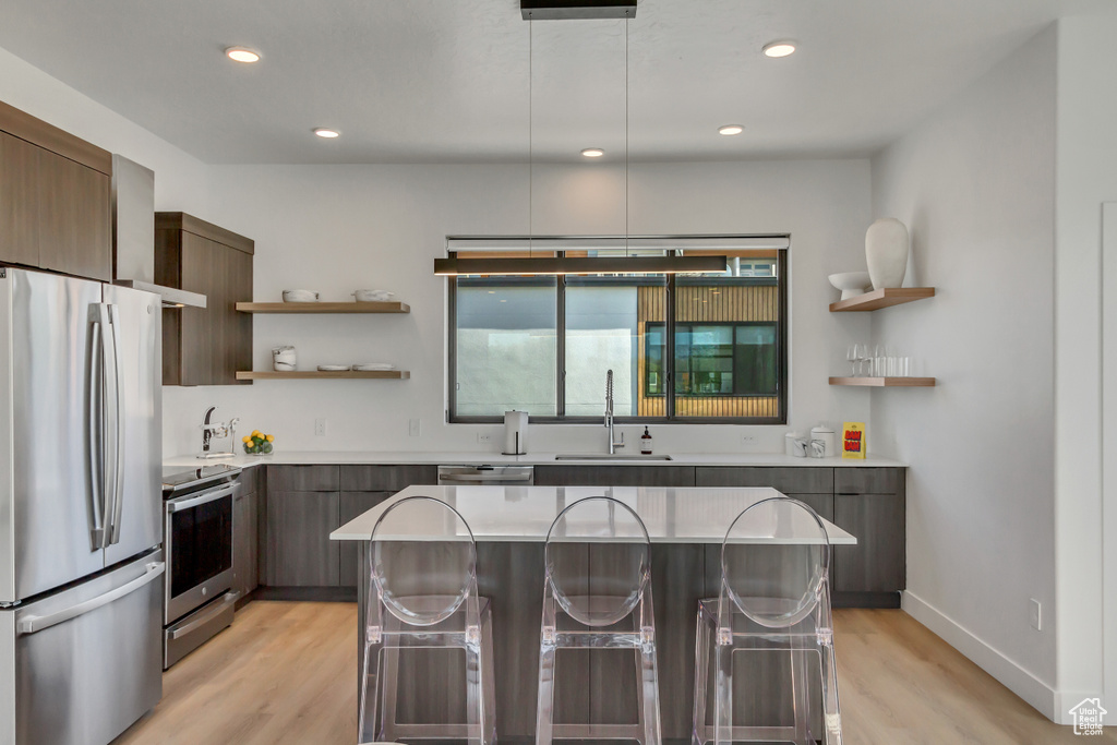Kitchen featuring hanging light fixtures, sink, stainless steel appliances, and light wood-type flooring
