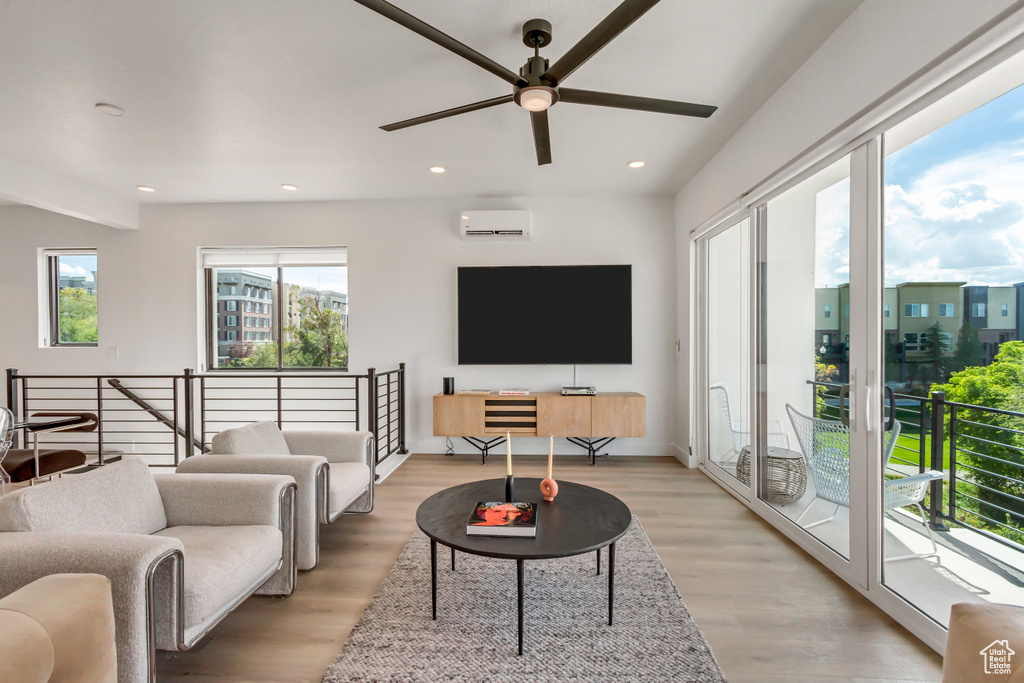 Living room with light hardwood / wood-style floors, ceiling fan, and a wall mounted air conditioner