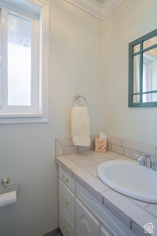 Bathroom featuring a healthy amount of sunlight, vanity with extensive cabinet space, and ornamental molding