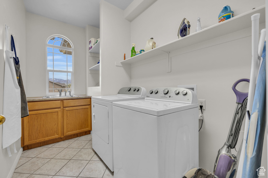Clothes washing area featuring separate washer and dryer, sink, and light tile flooring