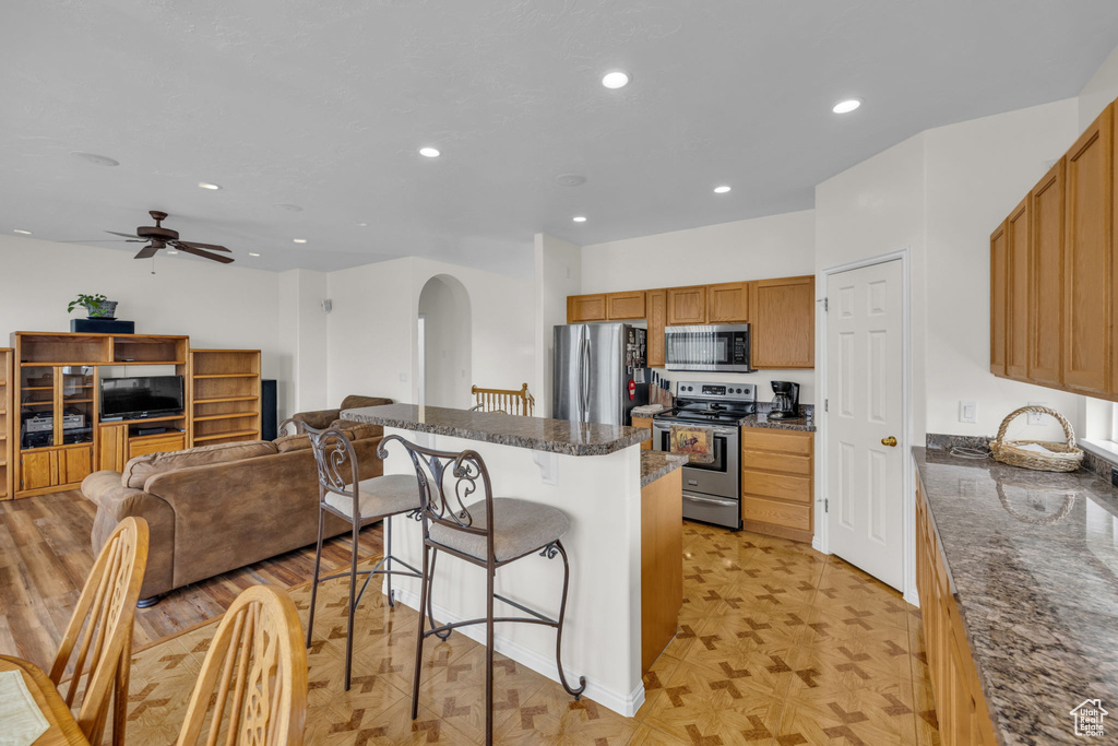 Kitchen featuring ceiling fan, light parquet flooring, a breakfast bar area, stainless steel appliances, and dark stone countertops
