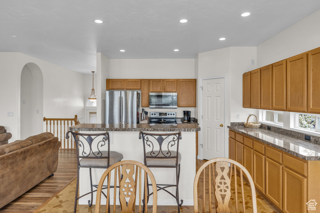 Kitchen with appliances with stainless steel finishes, a kitchen island, light hardwood / wood-style floors, a kitchen breakfast bar, and pendant lighting