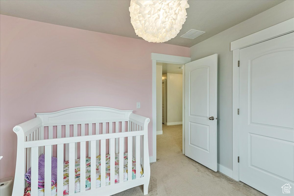 Carpeted bedroom featuring a notable chandelier and a nursery area