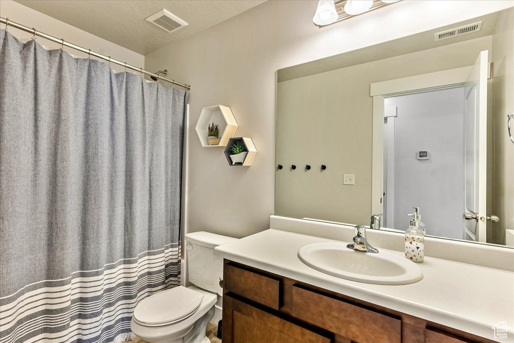 Bathroom featuring vanity with extensive cabinet space, toilet, and a textured ceiling