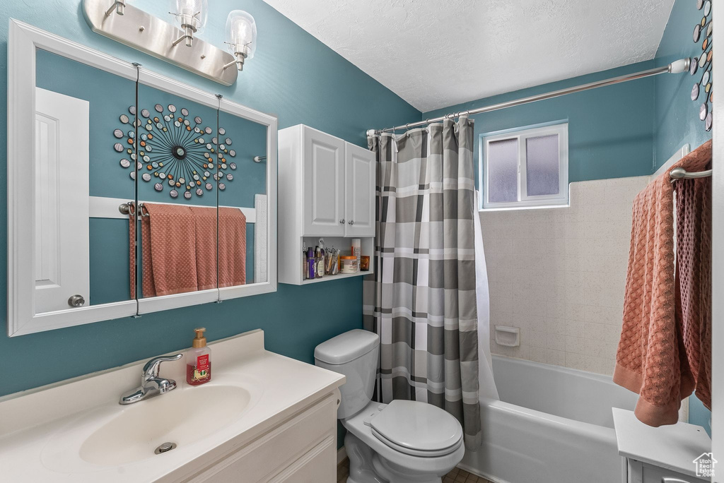 Full bathroom featuring oversized vanity, toilet, shower / tub combo with curtain, and a textured ceiling