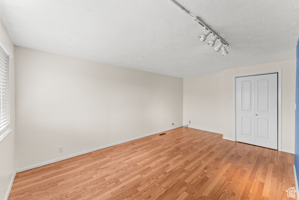 Empty room with track lighting, light hardwood / wood-style flooring, and a textured ceiling
