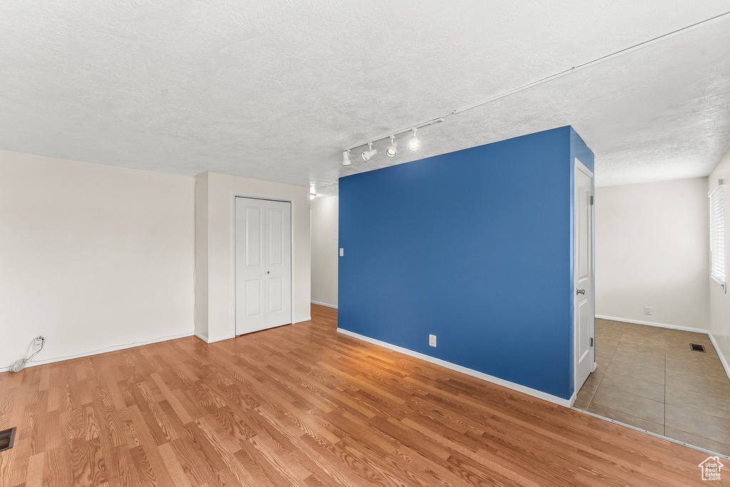 Empty room featuring light hardwood / wood-style floors, track lighting, and a textured ceiling