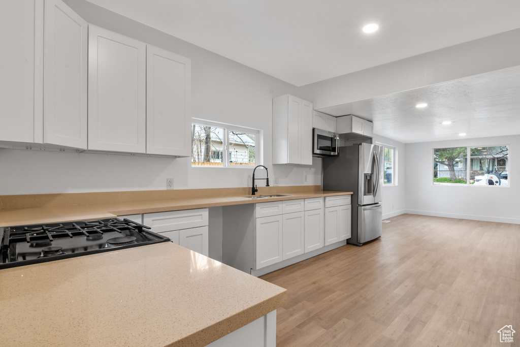 Kitchen with plenty of natural light, stainless steel appliances, white cabinetry, and light wood-type flooring