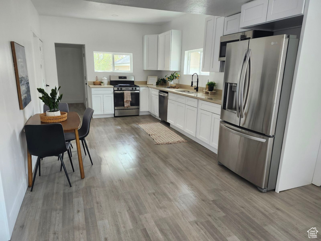 Kitchen with white cabinets, light hardwood / wood-style floors, and appliances with stainless steel finishes