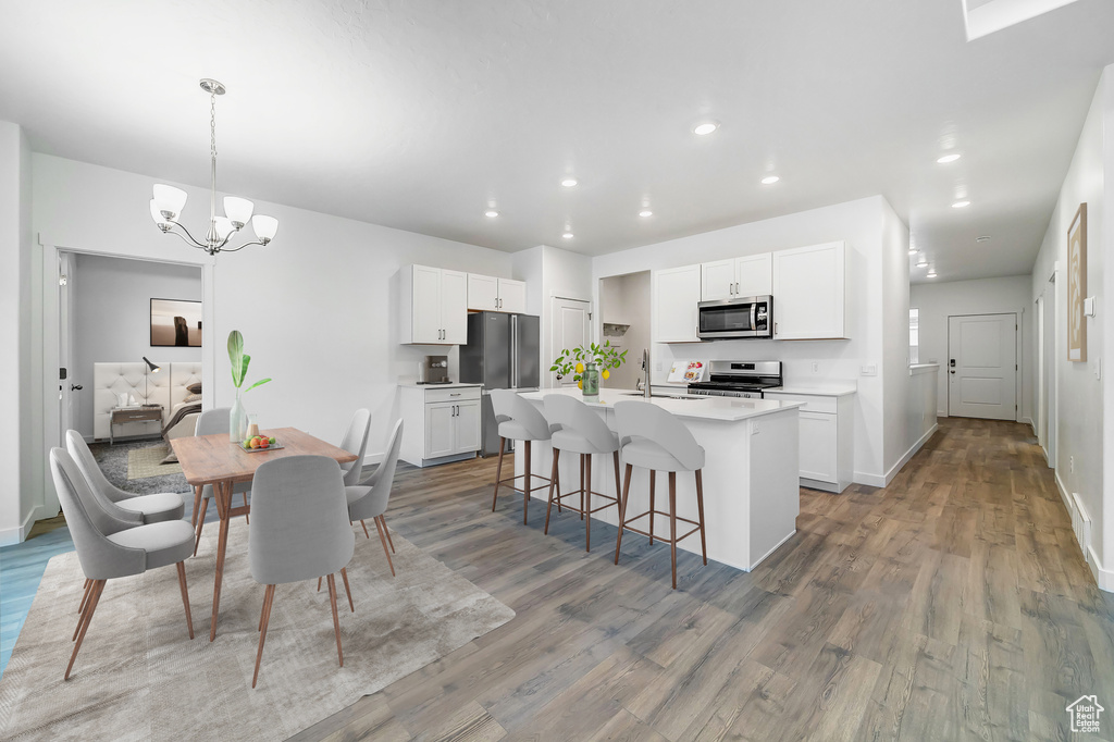 Kitchen with decorative light fixtures, appliances with stainless steel finishes, an island with sink, white cabinetry, and hardwood / wood-style floors