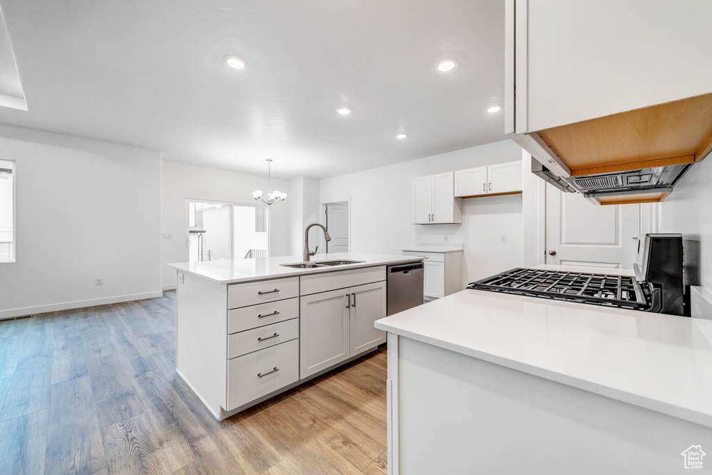 Kitchen featuring decorative light fixtures, white cabinetry, a center island with sink, sink, and light hardwood / wood-style floors