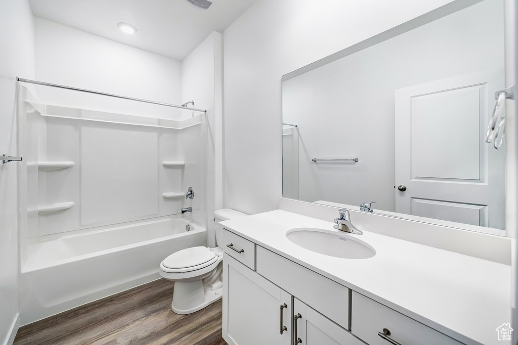 Full bathroom with shower / bathing tub combination, hardwood / wood-style floors, vanity with extensive cabinet space, and toilet