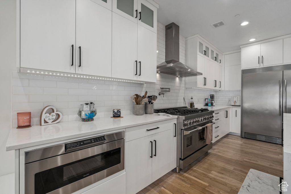 Kitchen featuring white cabinets, dark wood-type flooring, premium appliances, and wall chimney exhaust hood