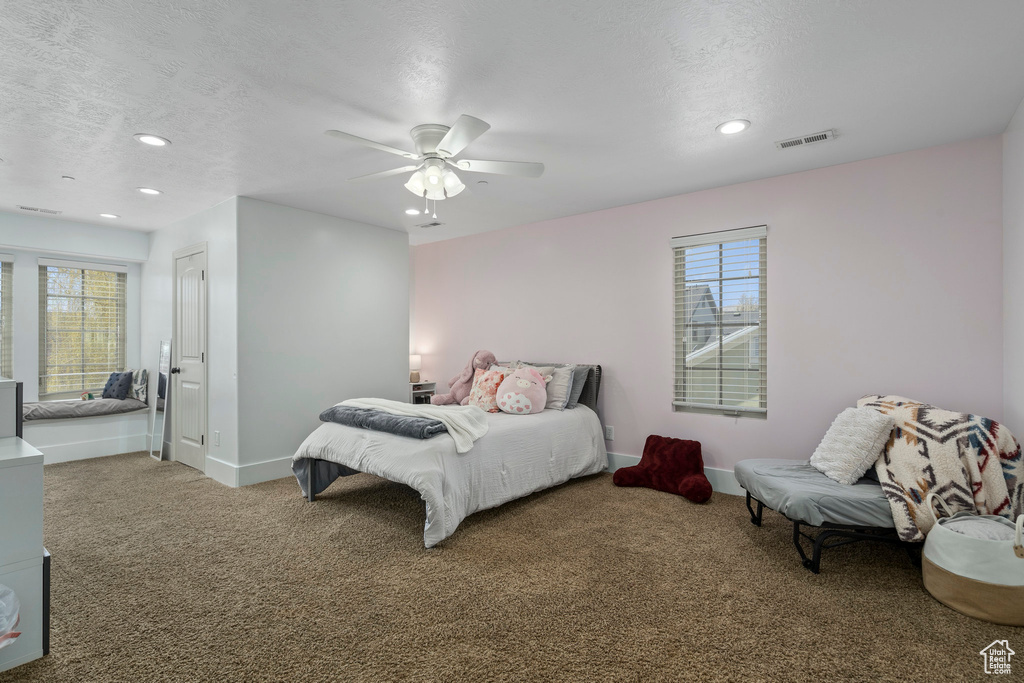 Carpeted bedroom featuring ceiling fan, multiple windows, and a textured ceiling