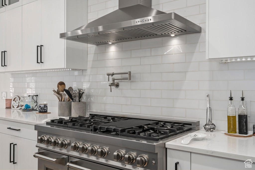 Kitchen featuring wall chimney exhaust hood, tasteful backsplash, white cabinets, and range with two ovens