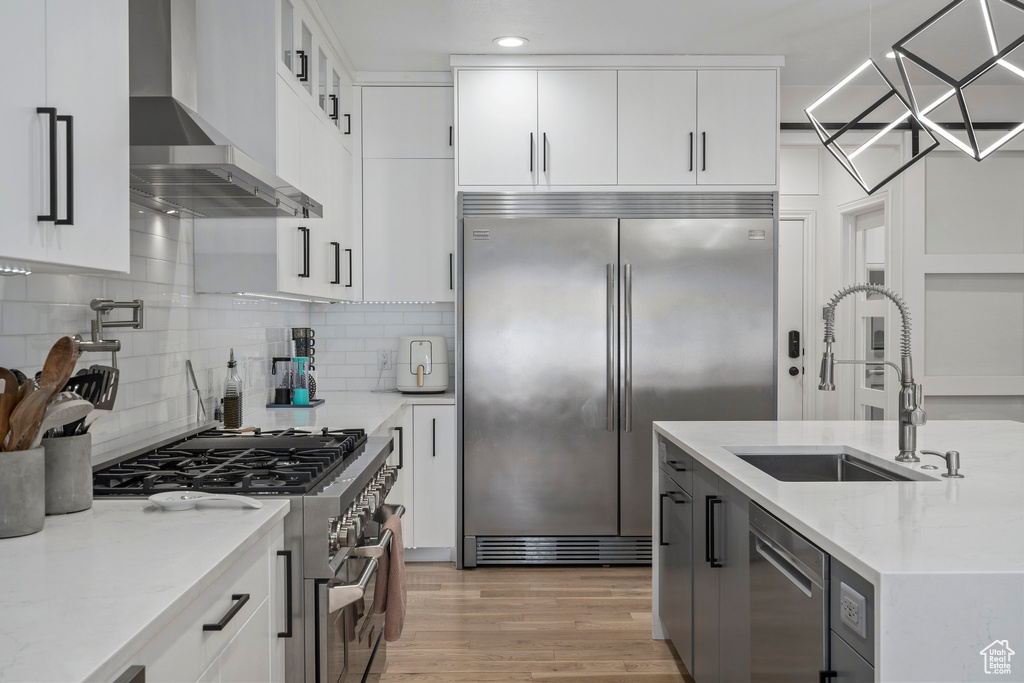 Kitchen with light hardwood / wood-style floors, backsplash, wall chimney exhaust hood, and high end appliances